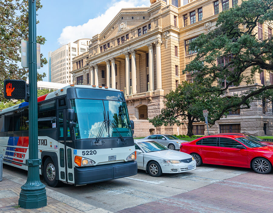 METRO local bus traveling through downtown Houston near the Harris County courthouses.
